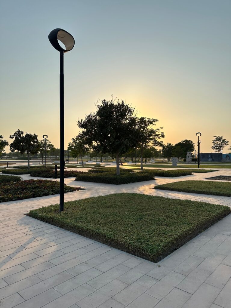 A serene city park at sunset with modern landscaping and lamp posts.