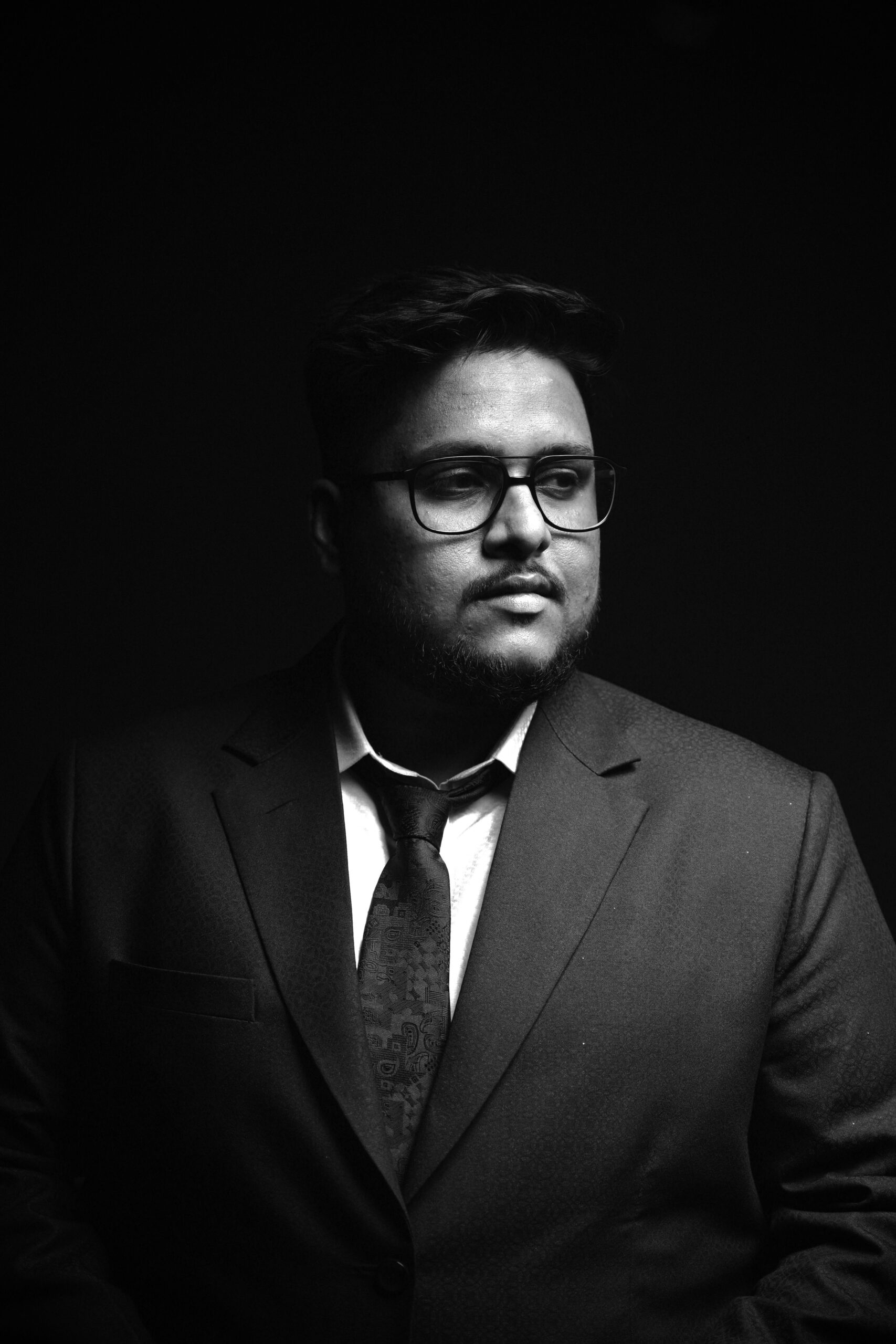 Black and white portrait of a man in a suit with glasses, conveying professionalism and style.