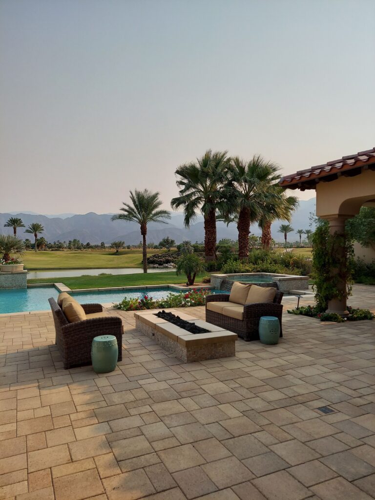 Serene outdoor patio with pool, wicker seating, and palm trees against mountain backdrop.